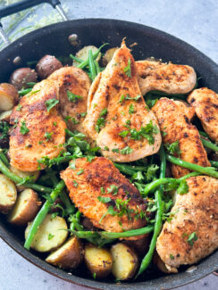 pan seared chicken in a black skillet with baby potatoes and green beans