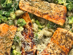 spinach gnocchi with broccoli and pan-seared salmon in a black skillet with parmesan cheese sprinkled on top