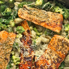 spinach gnocchi with broccoli and pan-seared salmon in a black skillet with parmesan cheese sprinkled on top