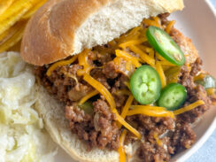 sloppy joes on a hamburger bun with cheddar cheese and sliced jalapeño peppers