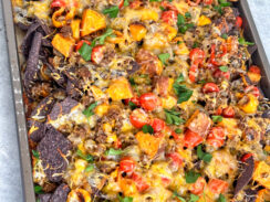 blue corn tortilla chips covered with melted cheese, chunks of roasted sweet potato, sweet peppers, cherry tomatoes on a sheet pan