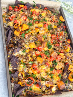blue corn tortilla chips covered with melted cheese, chunks of roasted sweet potato, sweet peppers, cherry tomatoes on a sheet pan