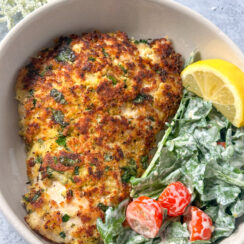 chicken milanese - lightly breaded chicken with fresh herbs and lemon in a white bowl with creamy arugula salad, cherry tomatoes, and a lemon wedge