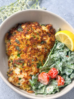chicken milanese - lightly breaded chicken with fresh herbs and lemon in a white bowl with creamy arugula salad, cherry tomatoes, and a lemon wedge