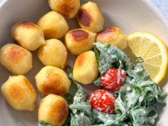 pan toasted alfredo stuffed gnocchi alongside a creamy arugula and cherry tomatoes salad with a lemon wedge in a white bowl