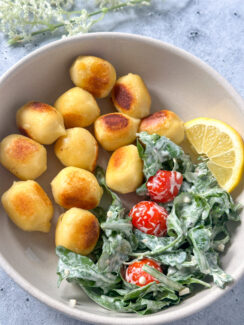 pan toasted alfredo stuffed gnocchi alongside a creamy arugula and cherry tomatoes salad with a lemon wedge in a white bowl