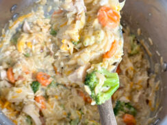 creamy orzo with chicken, broccoli, carrots, and cauliflower in a large pot with a wooden serving spoon