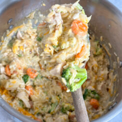 creamy orzo with chicken, broccoli, carrots, and cauliflower in a large pot with a wooden serving spoon