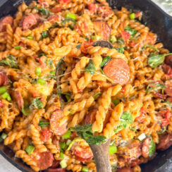 cheesy smoked sausage pasta with spinach in a black skillet with a wooden spoon.