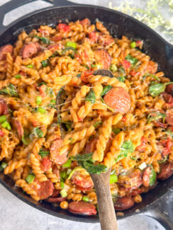 cheesy smoked sausage pasta with spinach in a black skillet with a wooden spoon.