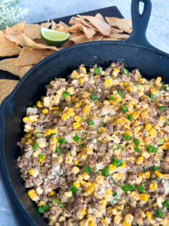 mexican hot corn dip in a cast iron skillet with gluten free tortilla chips and lime