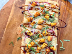 rectangular flatbread pizza with melted brie cheese, peaches, fresh basil leaves and balsamic drizzle on a wooden pizza serving tray