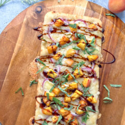 rectangular flatbread pizza with melted brie cheese, peaches, fresh basil leaves and balsamic drizzle on a wooden pizza serving tray