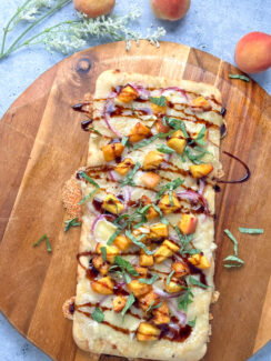 rectangular flatbread pizza with melted brie cheese, peaches, fresh basil leaves and balsamic drizzle on a wooden pizza serving tray