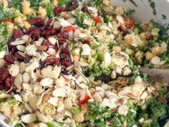 Costco copycat quinoa and celery salad with chickpeas, chopped kale, cherry tomatoes, red onion, parsley, dried cranberries, slivered almonds, and apple cider vinaigrette drizzle in a large bowl