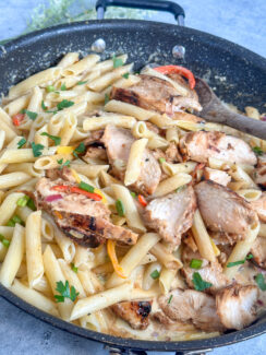 one pan jerk chicken pasta in a black skillet with penne pasta, red, yellow, and orange sautéed bell peppers and a creamy parmesan cheese sauce