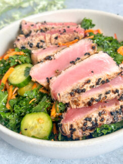 perfectly sesame seared ahi tuna slices on a bed of kale with cucumbers, shredded carrots, and sesame dressings