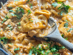 cheesy chicken enchiladas in a black cast iron skillet with tortilla strips in a creamy taco sauce topped with fresh cilantro