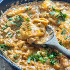 cheesy chicken enchiladas in a black cast iron skillet with tortilla strips in a creamy taco sauce topped with fresh cilantro