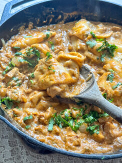 cheesy chicken enchiladas in a black cast iron skillet with tortilla strips in a creamy taco sauce topped with fresh cilantro