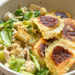 pan toasted lemon ravioli in a white bowl with creamy chicken caesar salad