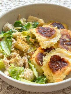 pan toasted lemon ravioli in a white bowl with creamy chicken caesar salad