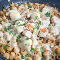 one pan french onion chicken pasta in a black skillet smothered in swiss cheese and freshly diced parsley leaves