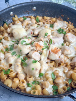 one pan french onion chicken pasta in a black skillet smothered in swiss cheese and freshly diced parsley leaves