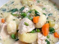 creamy chicken gnocchi soup in a white bowl with rotisserie chicken, carrots, peas, potatoes, and gnocchi