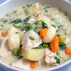 creamy chicken gnocchi soup in a white bowl with rotisserie chicken, carrots, peas, potatoes, and gnocchi