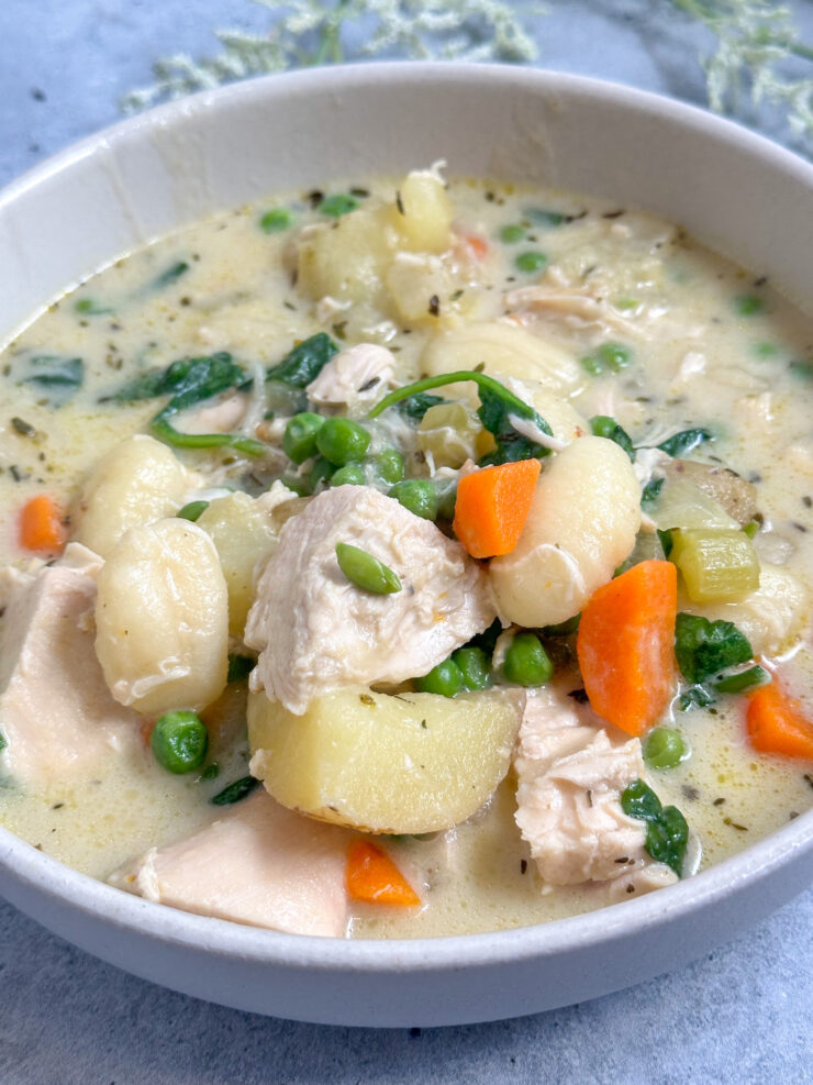 creamy chicken gnocchi soup in a white bowl with rotisserie chicken, carrots, peas, potatoes, and gnocchi