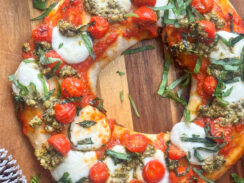 holiday pizza wreath made with refrigerated pizza dough, fresh mozzarella balls, cherry tomatoes, pizza sauce, and fresh shredded basil leaves on a wooden pizza board with winter pinecones