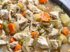 slow cooker chicken stew in a gray serving dish with tender chicken, carrots, celery, green beans, potatoes with a savory, hearty broth