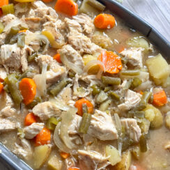 slow cooker chicken stew in a gray serving dish with tender chicken, carrots, celery, green beans, potatoes with a savory, hearty broth