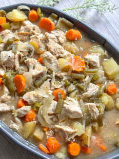 slow cooker chicken stew in a gray serving dish with tender chicken, carrots, celery, green beans, potatoes with a savory, hearty broth