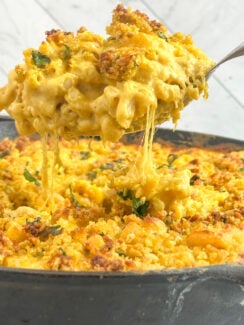 curry mac and cheese inspired by the viral tini's mac and cheese recipe with crispy curry cilantro breadcrumbs topping in a a black cast iron skillet with gooey gooey cheese on a spoon.