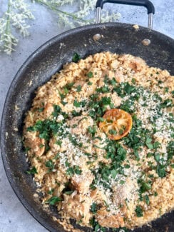 delicious one pan dinner creamy chicken caesar risotto in a black skillet with a lemon, parsley and parmesan cheese sprinkled on top