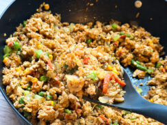 perfectly toasted garlic-ranch chicken fried rice in a black skillet with a gray serving spoon loaded with protein and family-approved for an easy recipe that everyone will love