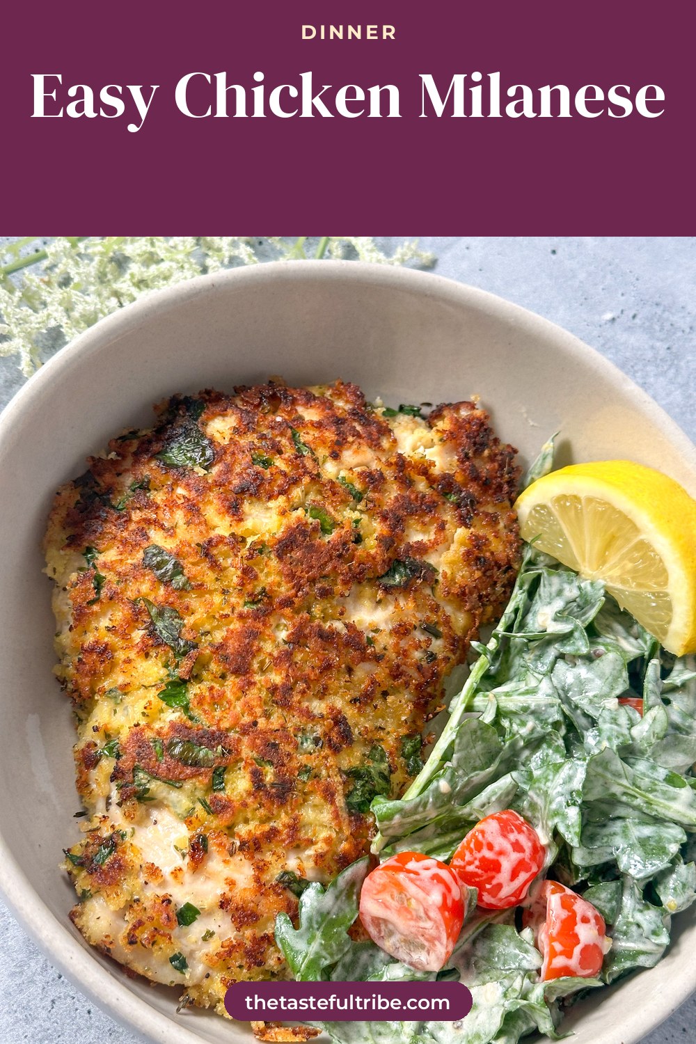 chicken milanese - lightly breaded chicken with fresh herbs and lemon in a white bowl with creamy arugula salad, cherry tomatoes, and a lemon wedge