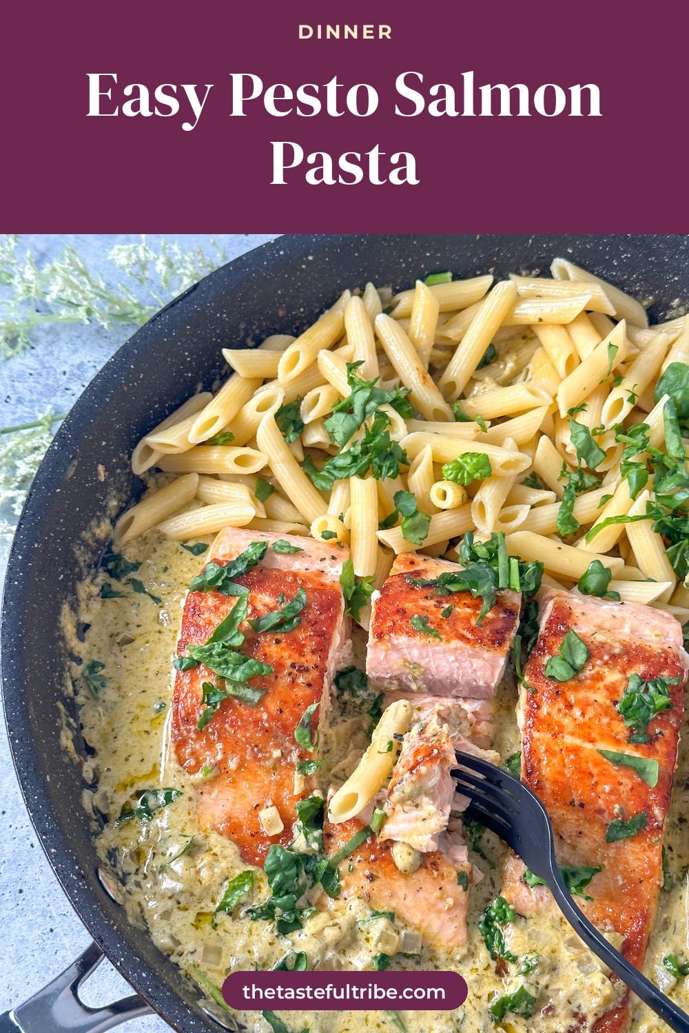 Seared salmon in a large skillet with a pesto cream sauce and penne pasta